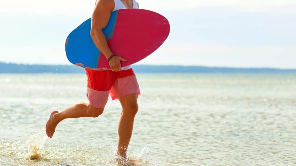 Skimboarder carrying a wooden skimboard on the beach