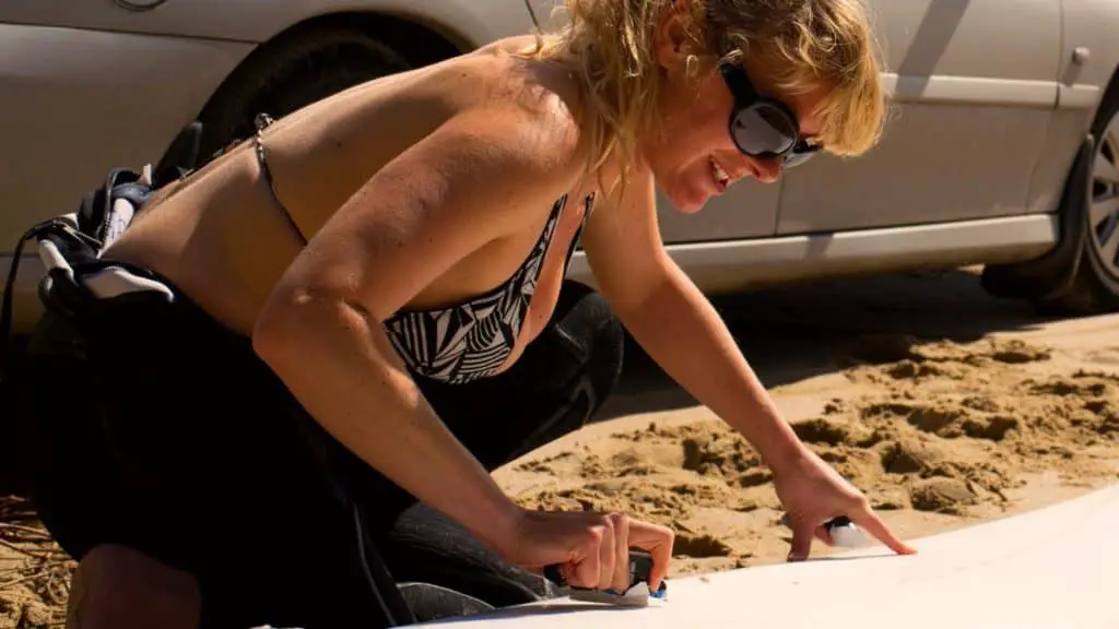 Woman waxing the top of her skimboard on the beach